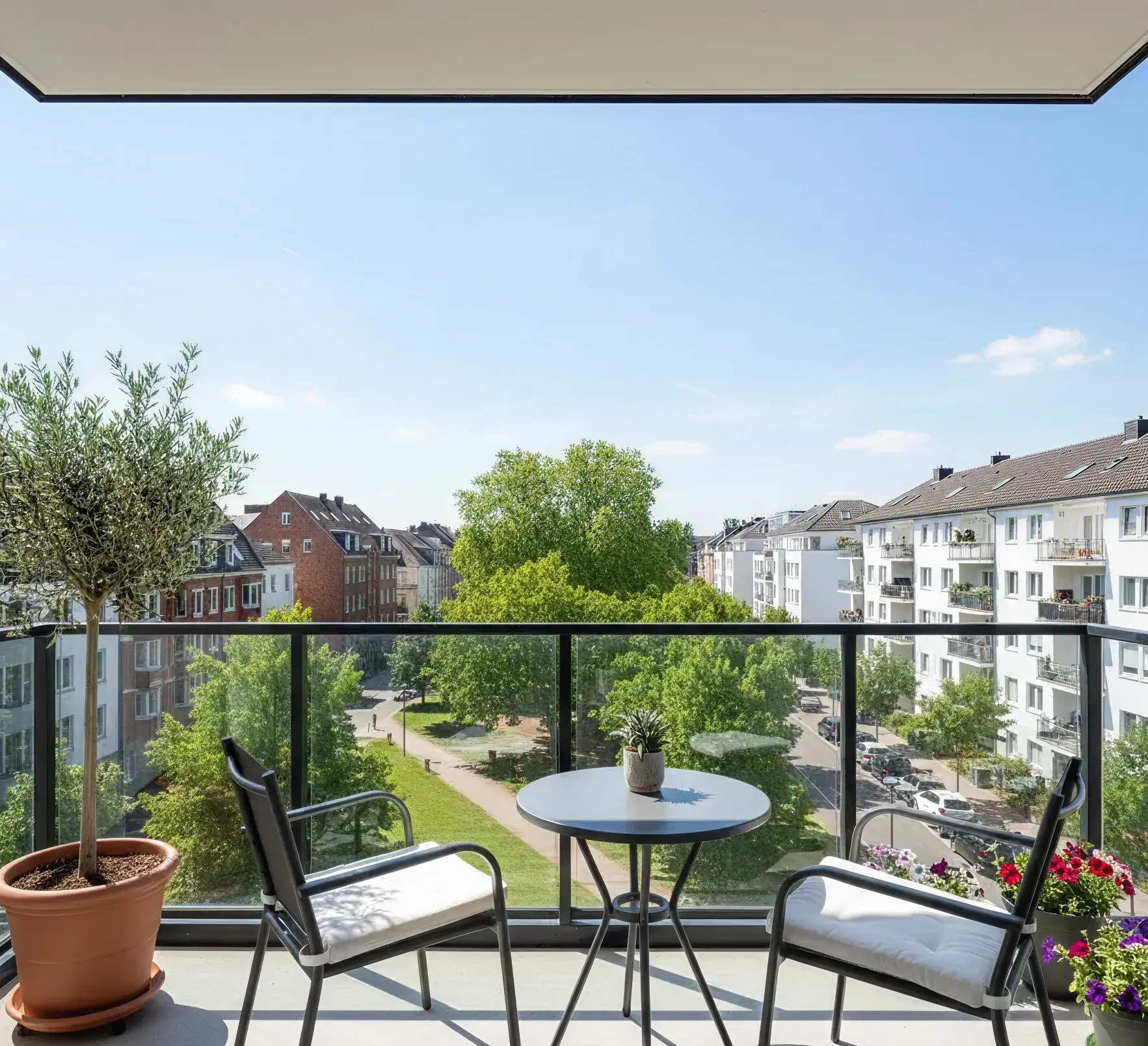 Blick von einem modernen Balkon mit Glasgeländer und Sitzgruppe auf eine gepflegte Grünanlage, ideal für entspanntes Wohnen und vermittelt durch Straub Immobilien.
